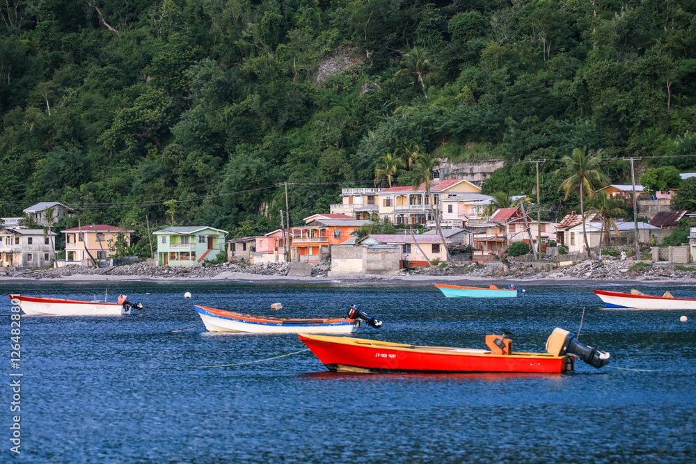 Fototapeta premium Boats bobbing gently in the blue waters off Dominica Island near colorful coastal houses