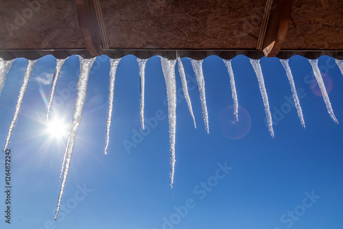 Icicles hanging from a roof on a sunny day. The sun is shining on the icicles