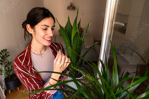 A young woman carefully inspecting her indoor plants with a soft smile, appreciating their growth and health photo