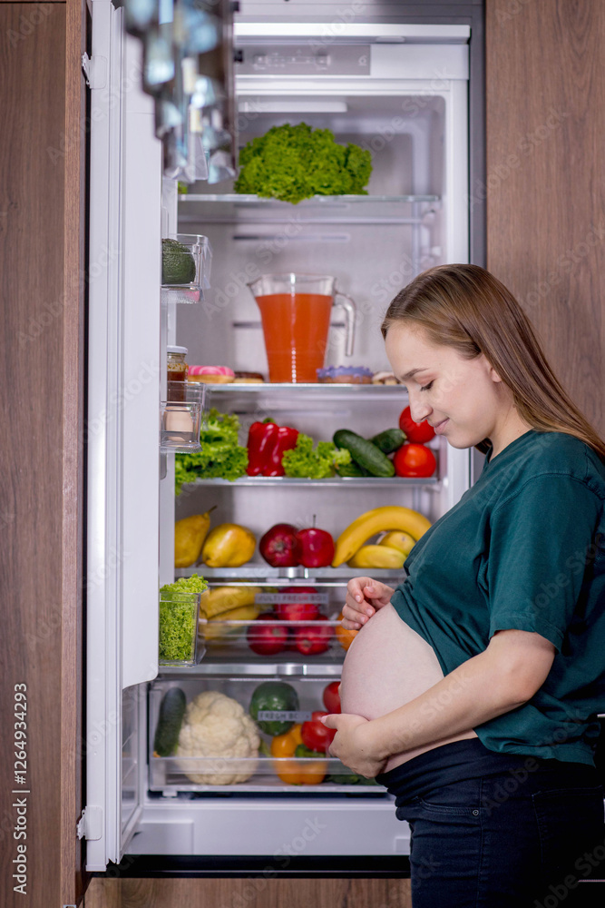 A pregnant woman stands by a fridge full of fruits and vegetables A pregnant woman stands by a fridge full of fruits and vegetables