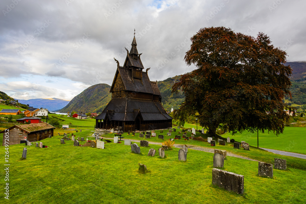 Hopperstad Stavkyrkje in South Norway, a historic wooden church surrounded by autumn trees and a peaceful graveyard. Hopperstad Stavkyrkje in South Norway, a historic wooden church surrounded by autumn trees and a peaceful graveyard.