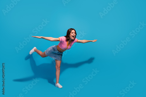 Wallpaper Mural Young woman joyfully posing against vibrant blue background in dynamic playful stance, wearing trendy pink and blue casual outfit Torontodigital.ca