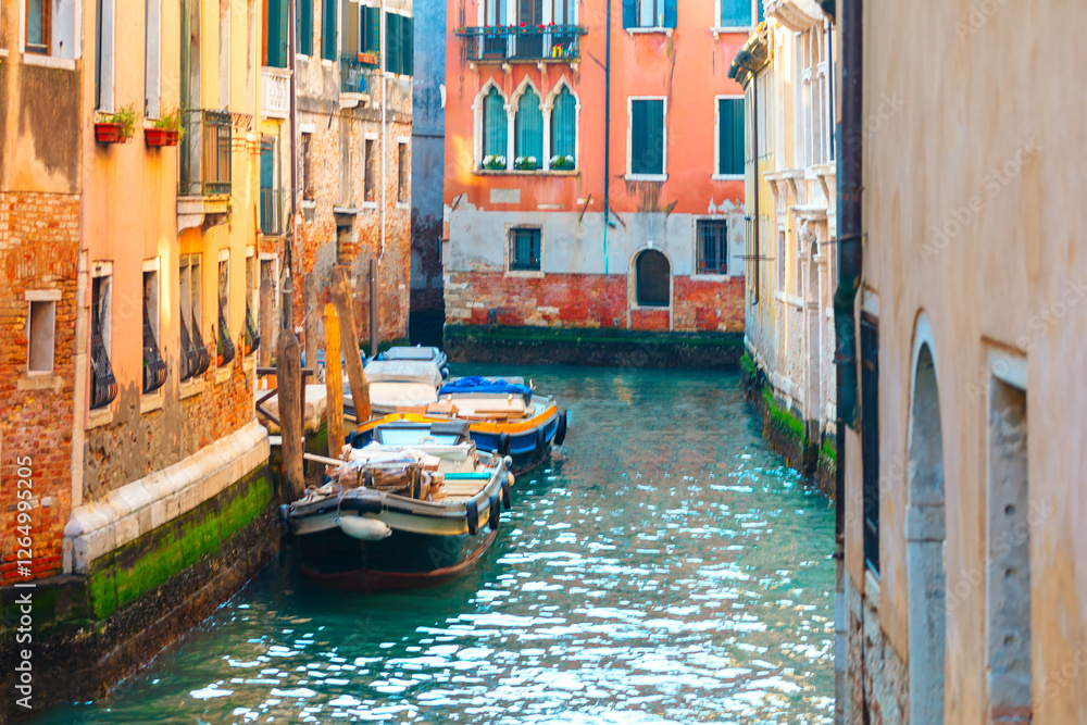Picturesque canal in Venice, Italy, with colorful buildings lining both sides and several boats moored along waterway. Vibrant hues of buildings and reflections in water capture Venice unique charm