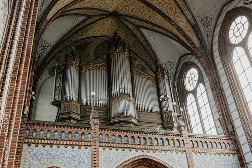 A grand pipe organ with intricate gold detailing set against the stunning vaulted ceiling and stained glass windows of a historic Gothic church interior
