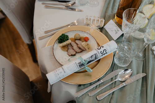  A beautifully set dining table with an elegantly plated gourmet dish featuring sliced meat, vegetables, crispy bread, and a decorative garnish, accompanied by a rolled menu tied with a ribbon