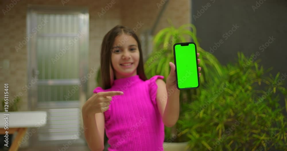 Young girl smiling and pointing at smartphone with green screen and chroma key, highlighting customizable display in a vibrant outdoor setting Young girl smiling and pointing at smartphone with green screen and chroma key, highlighting customizable display in a vibrant outdoor setting