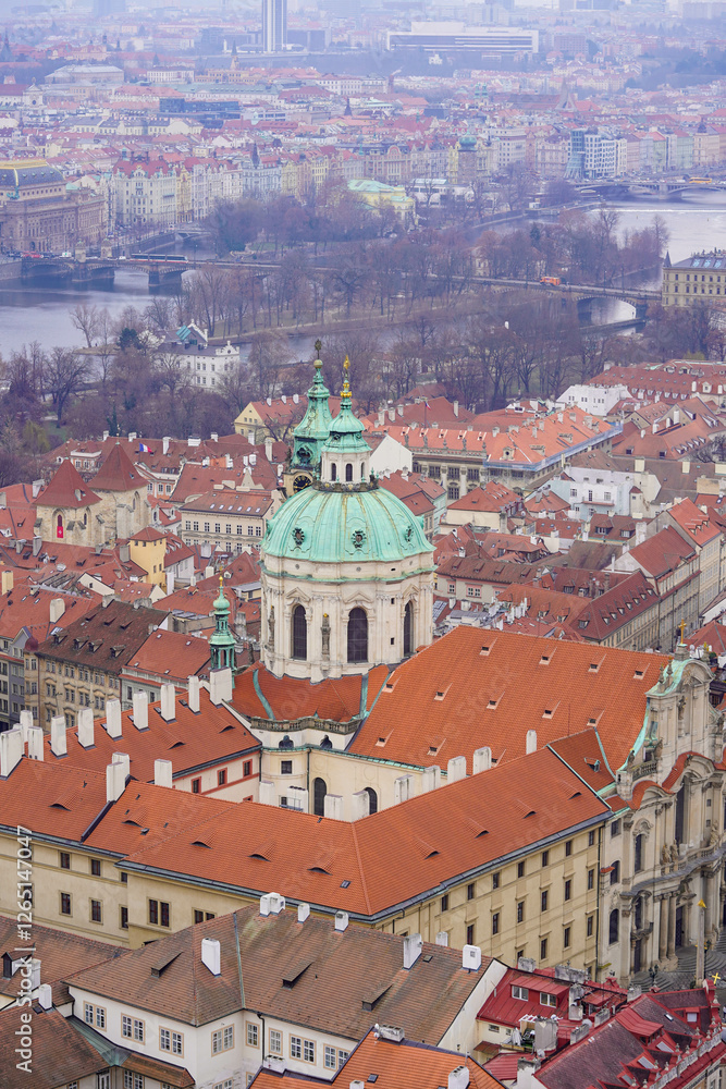 Fototapeta premium A panoramic view of a historic European city features a grand church with a green dome surrounded by red-roofed buildings
