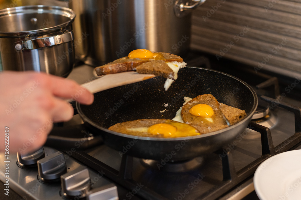 Man turns fried eggs with bread with wooden spatula. Man turns fried eggs with bread with wooden spatula.