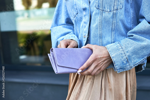 Obraz na płótnie Person holding stylish lavender clutch, wearing denim jacket, beige skirt, casual chic fashion concept w salonie