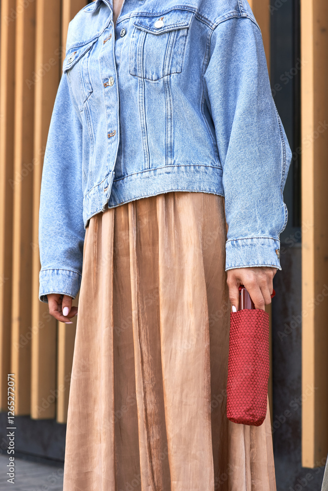 Stylish woman wearing denim jacket and flowing skirt with red umbrella accessory, modern fashion concept