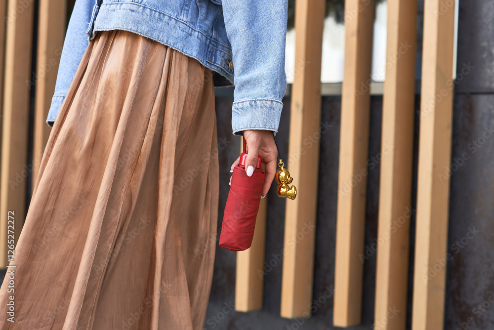 Fashionable person holding red umbrella with golden keychain while walking in urban setting, stylish accessory concept