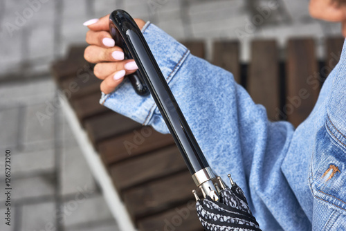 Obraz na płótnie Hand holding stylish umbrella, black handle, denim jacket, rainy day, urban setting, protective accessory, casual fashion, weather concept w salonie