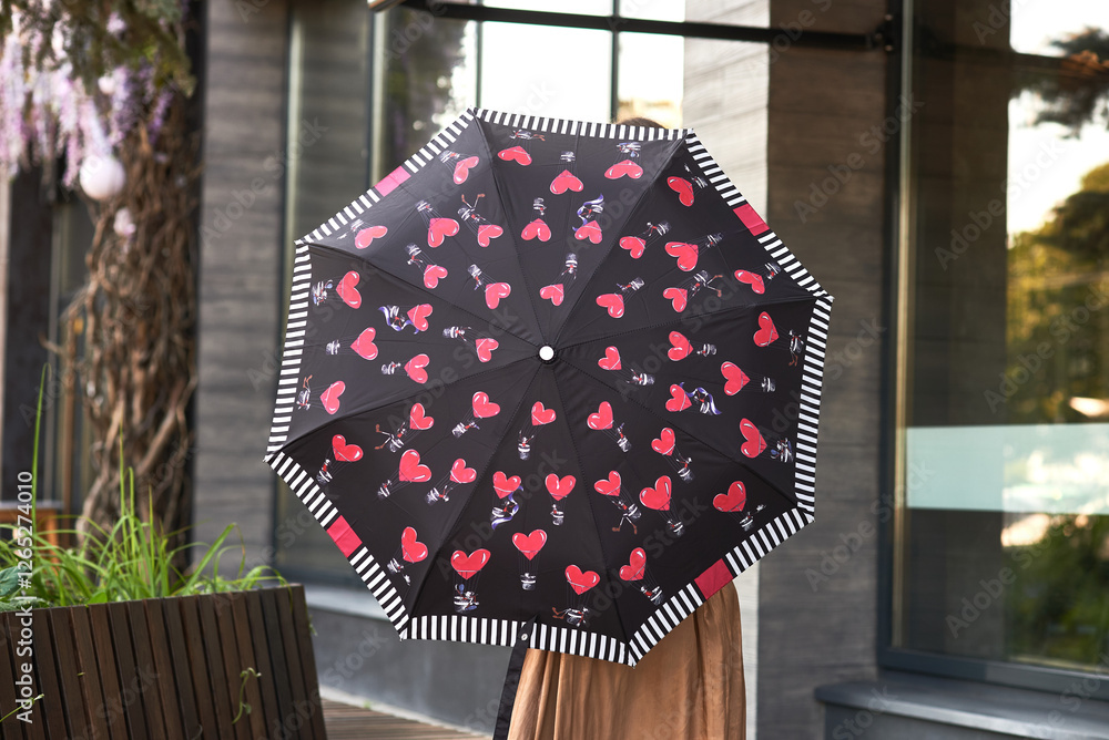 Black umbrella with red heart pattern held by person outside modern building, heart-themed accessory concept
