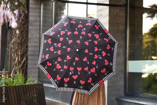 Obraz na płótnie Black umbrella with red heart pattern held by person outside modern building, heart-themed accessory concept w salonie