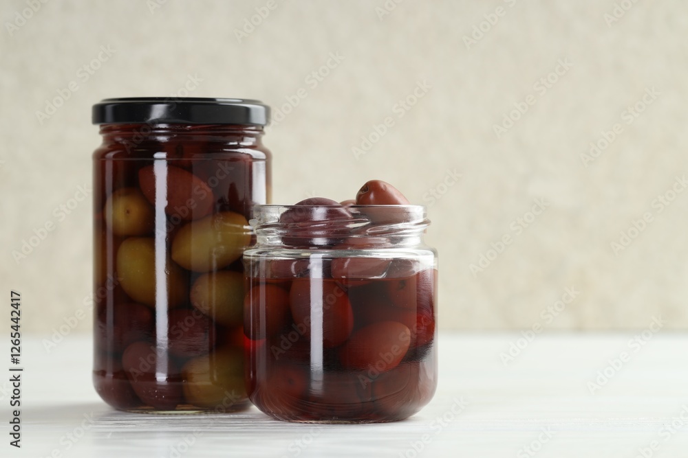 Pickled olives in glass jars on white wooden table, closeup. Space for text Pickled olives in glass jars on white wooden table, closeup. Space for text