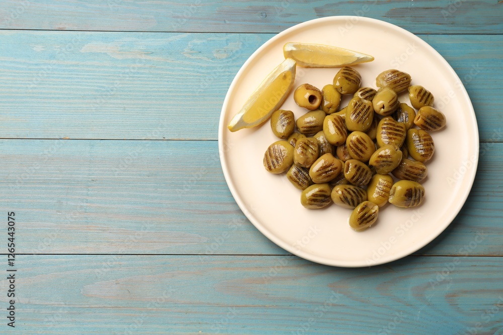 Grilled green olives and lemon wedges on light blue wooden table, top view. Space for text Grilled green olives and lemon wedges on light blue wooden table, top view. Space for text