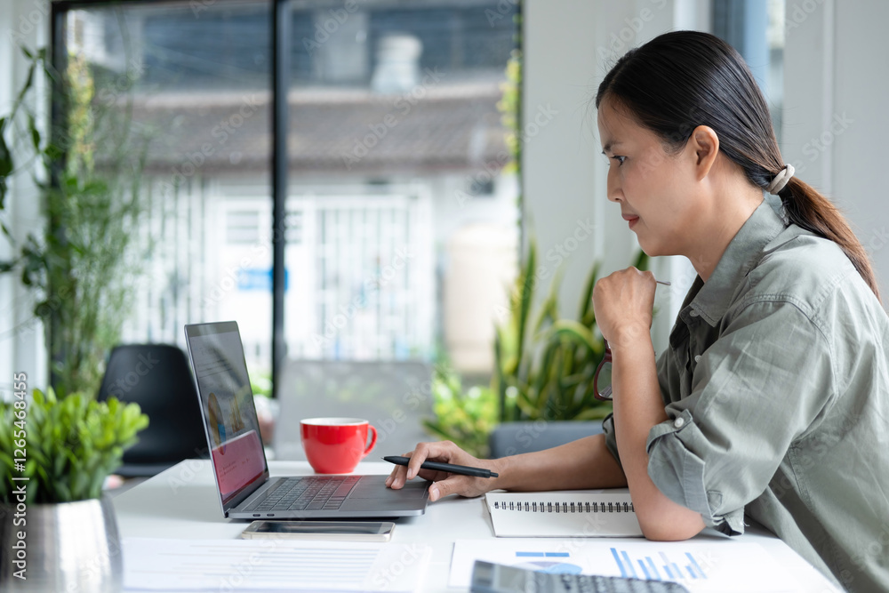 Businesswoman sitting at desk on couch in workplace or at home working on laptop and analyzing data on charts and graphs and writing on papers to make business plan and strategies for company Businesswoman sitting at desk on couch in workplace or at home working on laptop and analyzing data on charts and graphs and writing on papers to make business plan and strategies for company