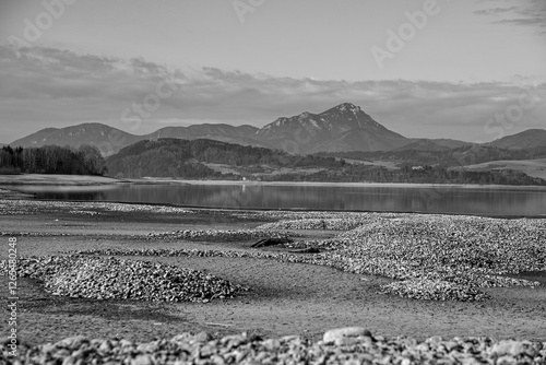 Rocky mounds emerging from drying liptovská mara lake with choč mountain reflecting in remaining water in slovakia photo