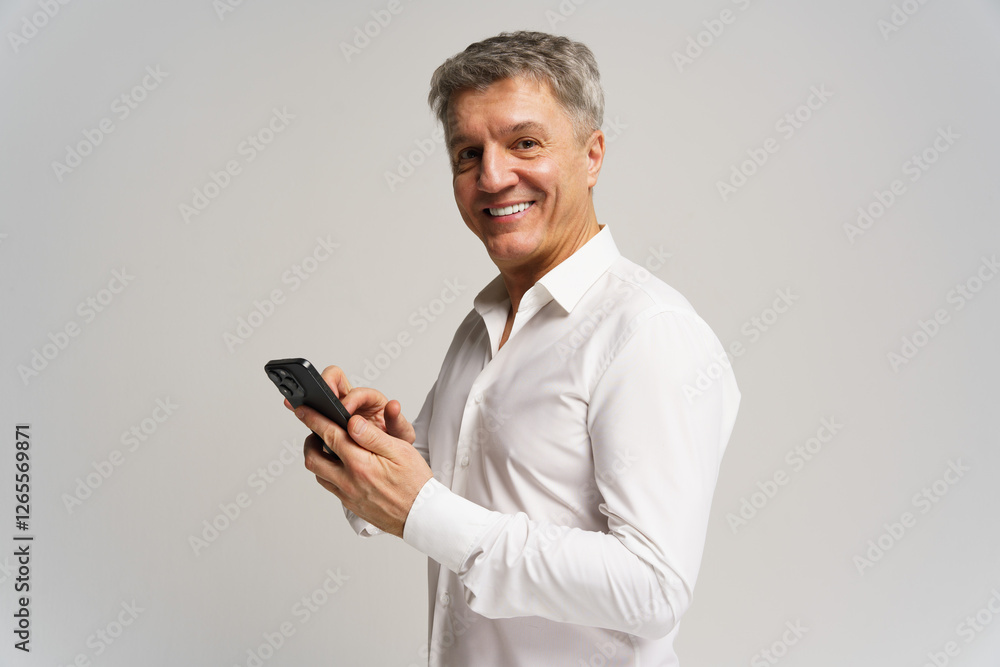 Middle-aged man dressed in white shirt happily using smartphone in a bright studio setting Middle-aged man dressed in white shirt happily using smartphone in a bright studio setting