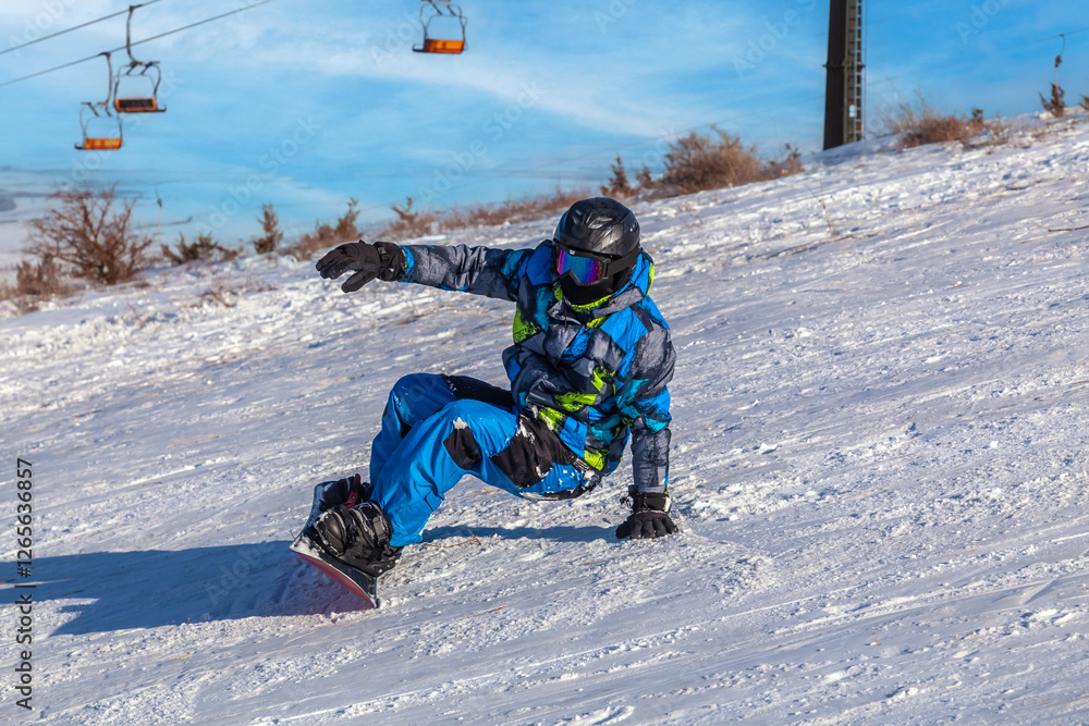 Snowboarder falls in snow. Snowboarder lies on the ground in a jacket. Snowboarder wears helmet and glasses. Snowboarder falls in snow. Snowboarder lies on the ground in a jacket. Snowboarder wears helmet and glasses.