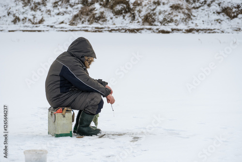 Obraz na plátně Traditional Ice Fishing: Angler Sitting on the Ice with a Rod