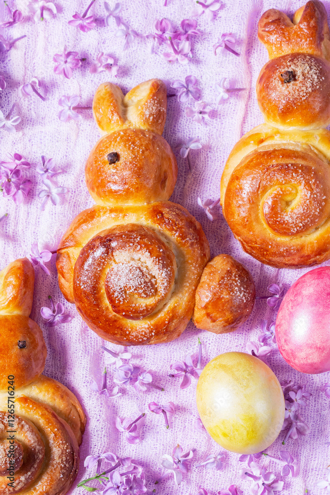Easter composition made of sweet buns in the shape of a rabbit, eggs and lilacs.