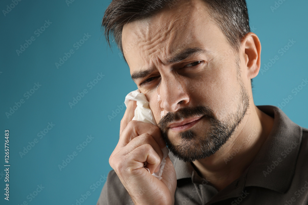 Fototapeta premium Sad man with paper tissue crying on light blue background, space for text
