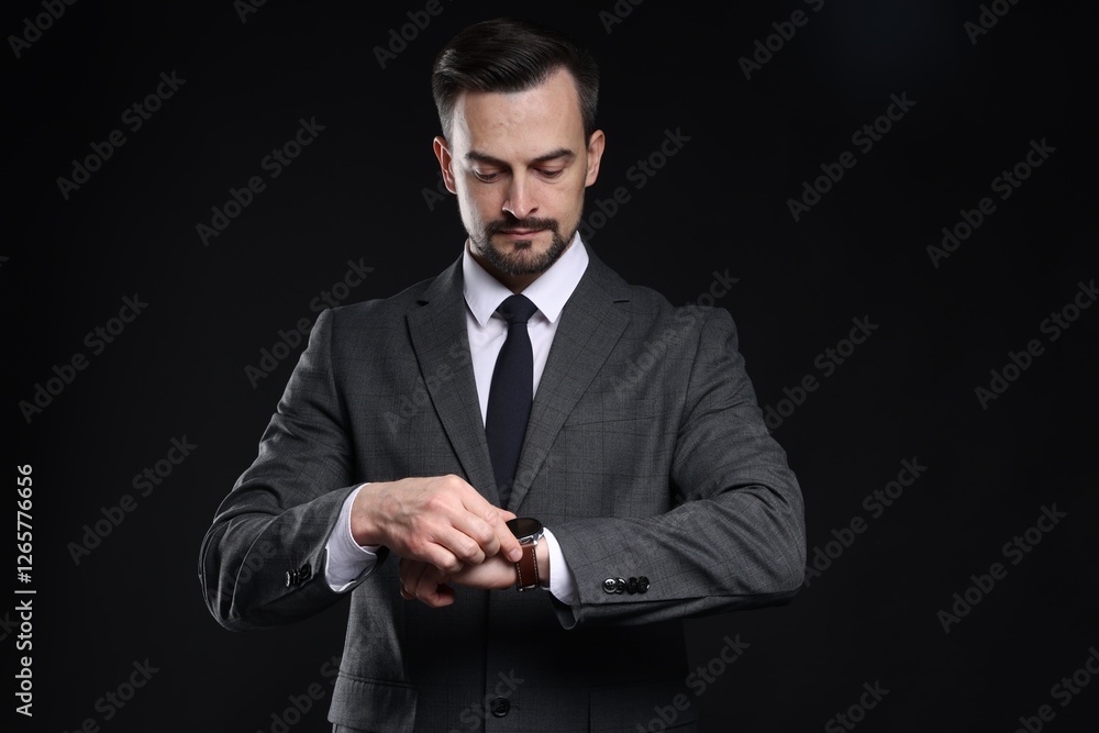 Handsome man in classic suit checking time on black background Handsome man in classic suit checking time on black background
