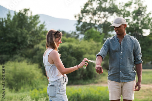 Quadro em tela Young couple spraying tick repellent on her legs and arms during a summer nature