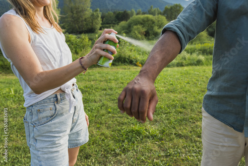 Fotografia Young couple spraying tick repellent on her legs and arms during a summer nature