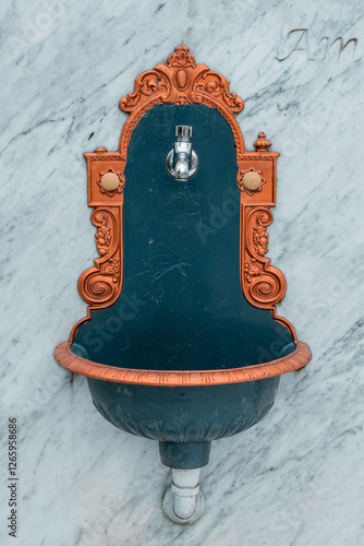 Obraz na płótnie Front view of a vintage ornamental water basin and faucet mounted on a marble wall. Golden ornaments at side. w salonie