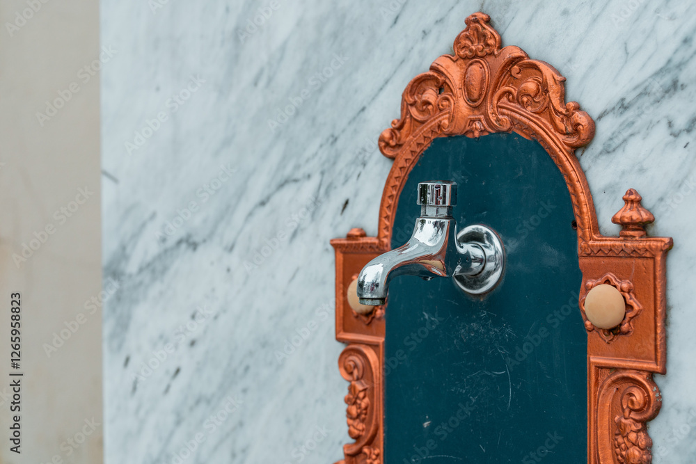 Side view of a vintage ornamental water basin and faucet mounted on a marble wall. Golden ornaments at side.