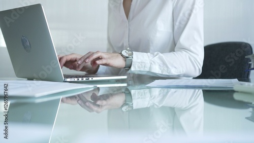 Obraz na płótnie Businesswoman in white blouse typing on laptop at glass desk while sitting in bright office, showcasing productivity and modern work environment. Businesspeople concept w salonie
