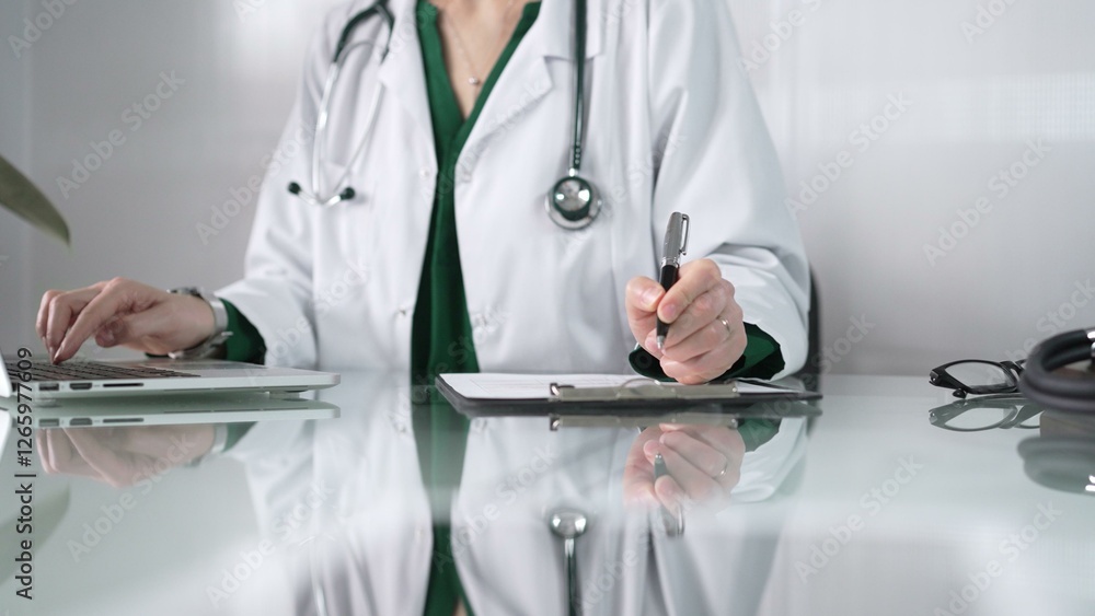 Woman doctor using a clipboard and taking notes on glass desk in a medical office, close-up view. Medicine concept Woman doctor using a clipboard and taking notes on glass desk in a medical office, close-up view. Medicine concept
