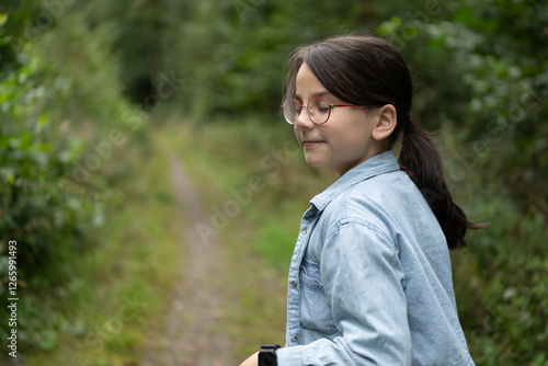 Little cute cheerful girl in glasses and a T-shirt on a path in the middle of a summer forest. Concept of children's active travel in nature