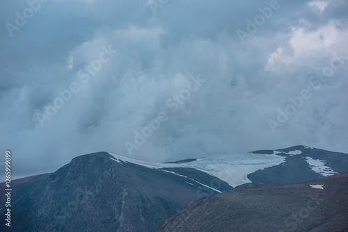 Dark atmospheric alpine landscape with big rocky mountain silhouettes with sn...
