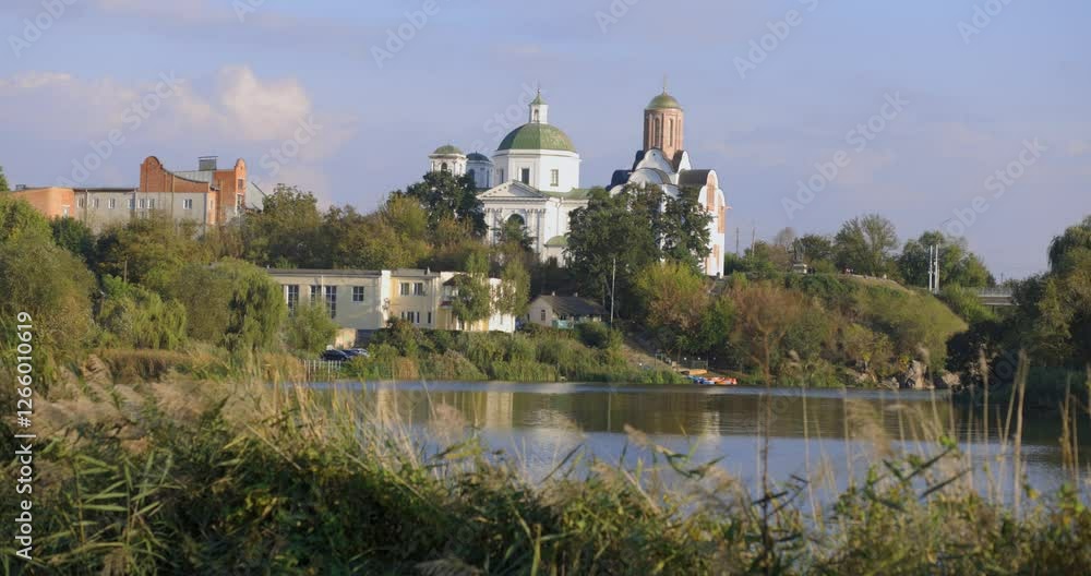 A peaceful riverside scene with lush greenery, a bridge, and historic buildings, including a church with a dome. The calm water reflects the serene atmosphere of the sunny day. A peaceful riverside scene with lush greenery, a bridge, and historic buildings, including a church with a dome. The calm water reflects the serene atmosphere of the sunny day.