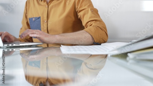 Businessman wearing yellow shirt is typing on laptop keyboard, preparing taxes and audit reports on glass desk. Taxes, audit in business