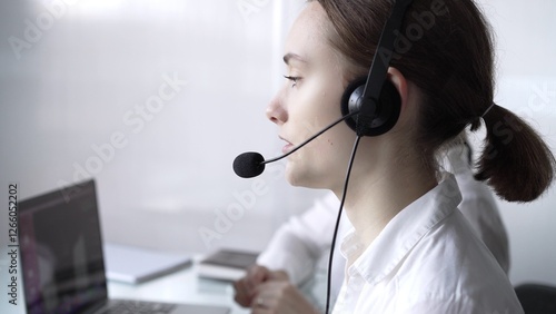 Young female call center operator in white blouse is assisting clients online, providing customer support and answering inquiries. Business call center