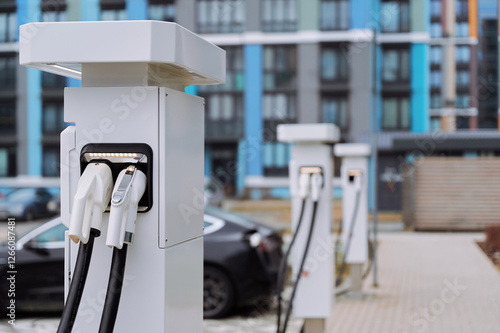 Line of electric vehicle charging stations installed in a modern parking lot. Vibrant building facade in the background adds a colorful touch to the urban landscape