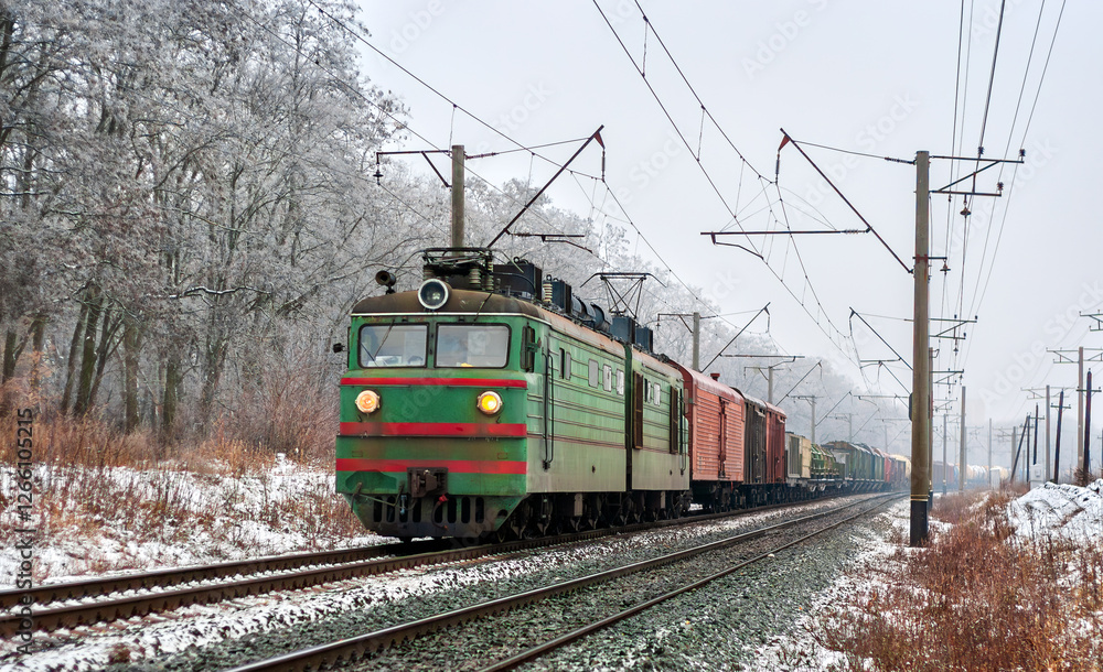 Obraz premium Old Soviet electric locomotive with a long freight train in winter in Kyiv Oblast of Ukraine