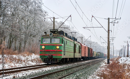 Old Soviet electric locomotive with a long freight train in winter in Kyiv Oblast of Ukraine photo