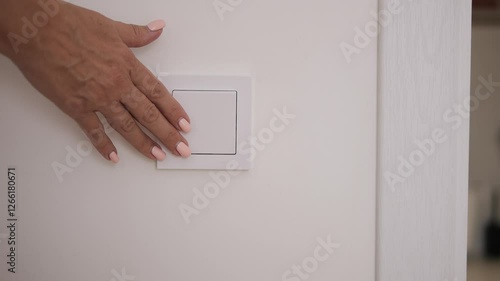 Female hand turns off light using wall switch Closeup of hand pressing switch to stop light in room Concept of saving energy turning off light reducing electricity use and conserving power efficiently