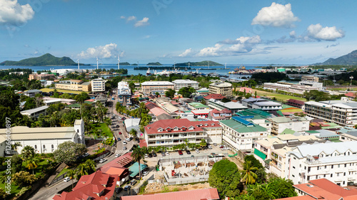 A cityscape with buildings, a port, wind turbines, and distant mountains under a clear sky. Seychelles, Mahe. Victoria.