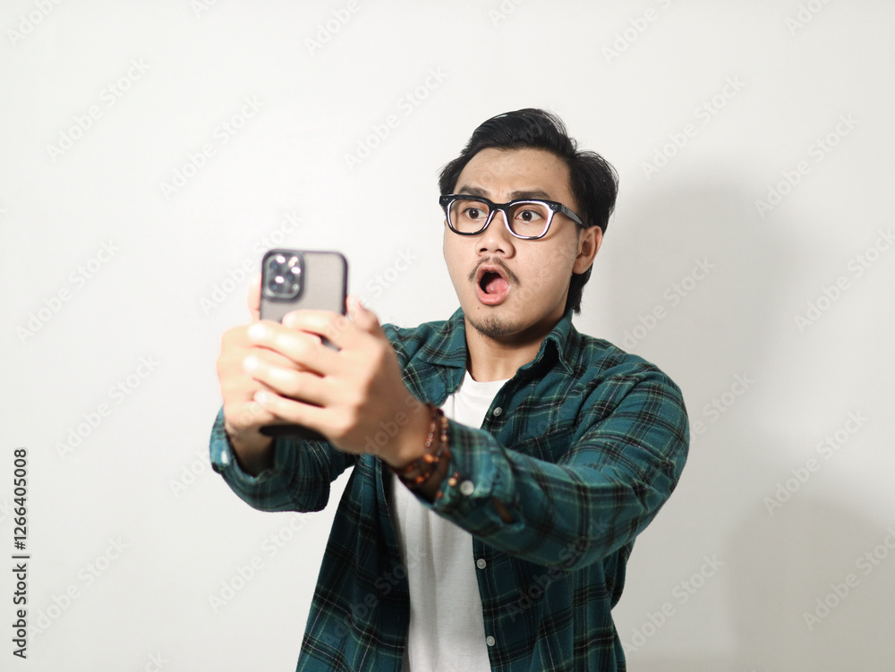 Adult Asian man typing on his mobile phone with excited expression isolated on white background Adult Asian man typing on his mobile phone with excited expression isolated on white background
