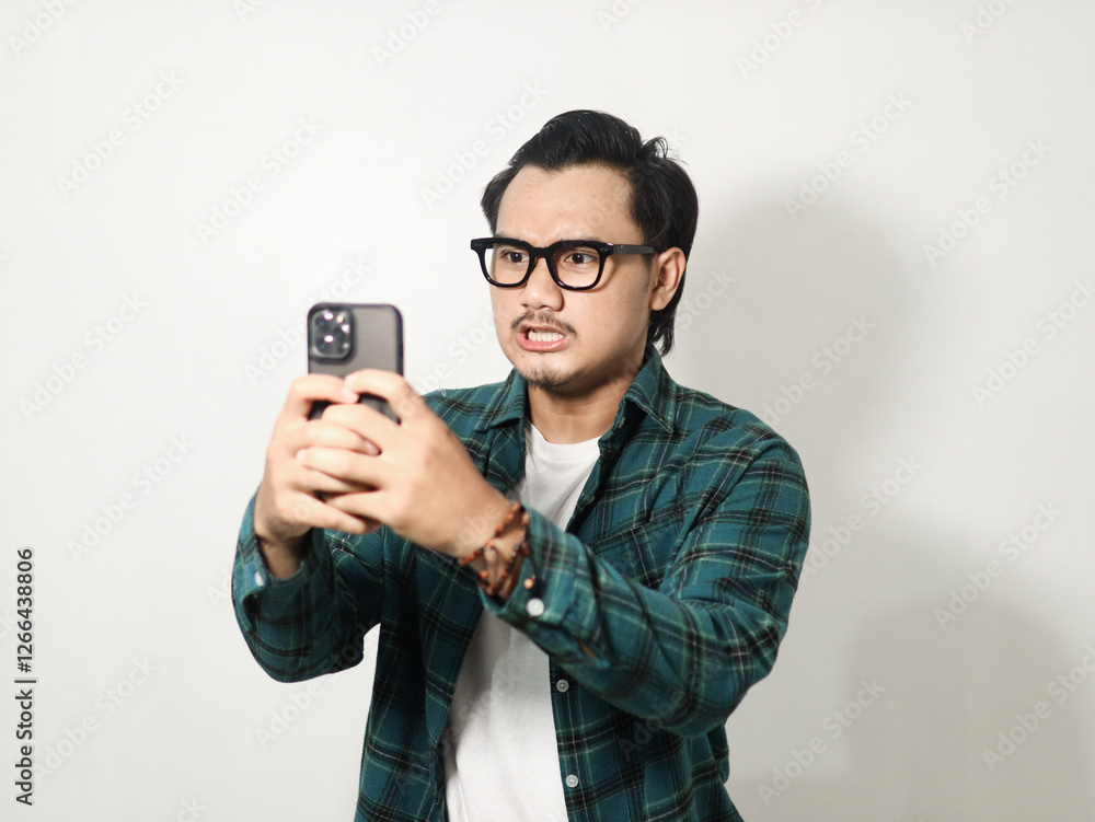 Adult Asian man is typing on his mobile phone with angry expression isolated on white background Adult Asian man is typing on his mobile phone with angry expression isolated on white background