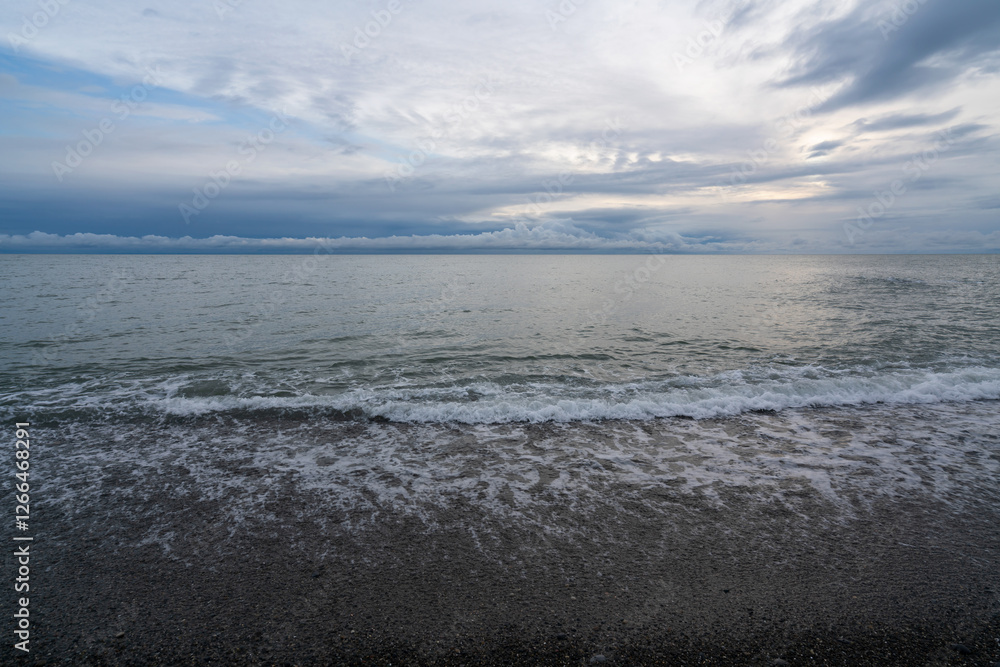 An incoming wave on the Black Sea and a pebble beach on the Sochi coast on a summer day with clouds, Sochi, Krasnodar Territory, Russia An incoming wave on the Black Sea and a pebble beach on the Sochi coast on a summer day with clouds, Sochi, Krasnodar Territory, Russia