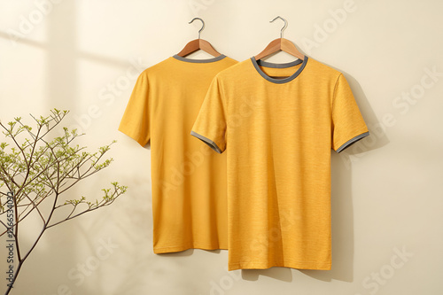 Two Yellow T Shirts Hanging On Wooden Hangers With A Neutral Background. Yellow