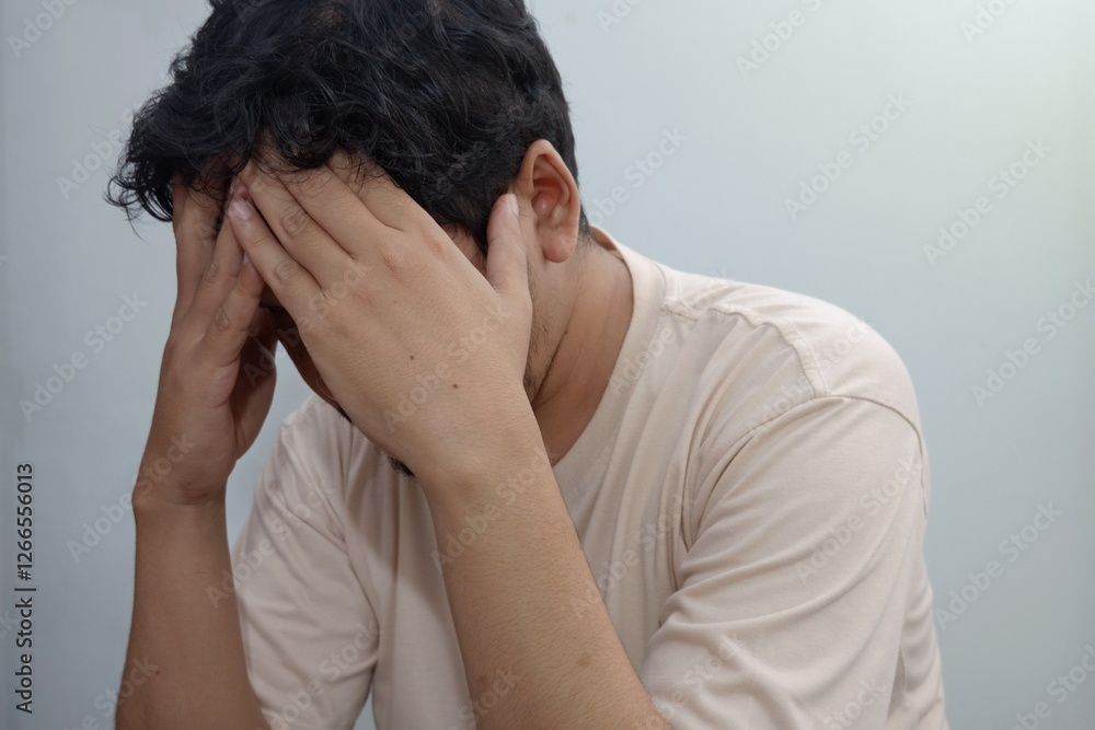 Southeast Asian Man Holding Head in Hands, Depicting Stress or Sadness Southeast Asian Man Holding Head in Hands, Depicting Stress or Sadness