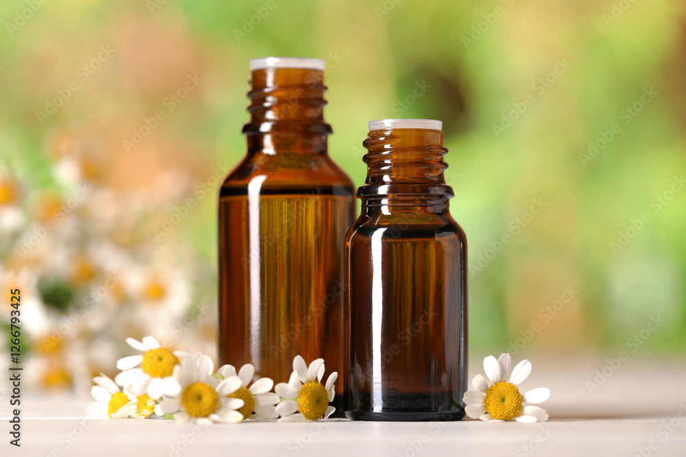 Bottles of essential oil and chamomile flowers on white wooden table against blurred background, closeup Bottles of essential oil and chamomile flowers on white wooden table against blurred background, closeup